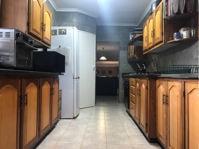 A functional galley-style kitchen featuring traditional wooden cabinetry, granite countertops, and tiled finishes throughout.