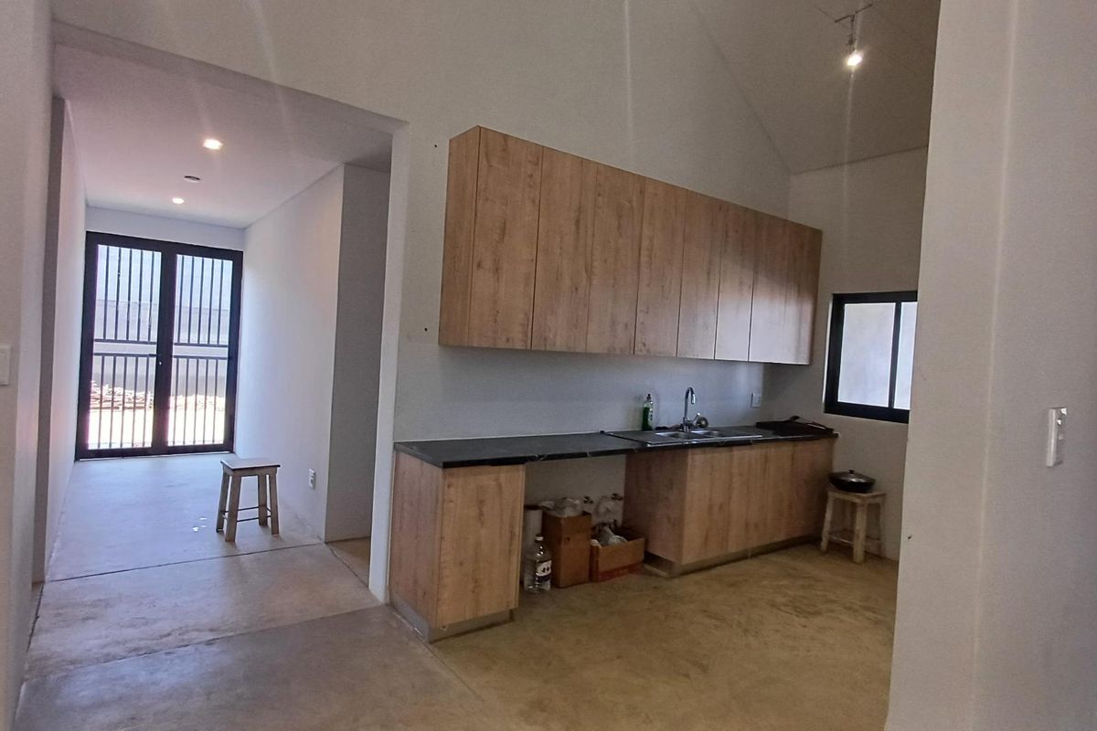 A functional kitchen area featuring wood-look cabinetry, dark countertops, and a stainless steel sink, set within an open-plan space with vaulted ceilings.
