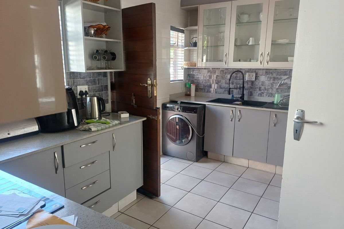 A functional kitchen featuring grey cabinetry, tiled splashbacks, a double sink with a modern faucet, and integrated space for laundry appliances.