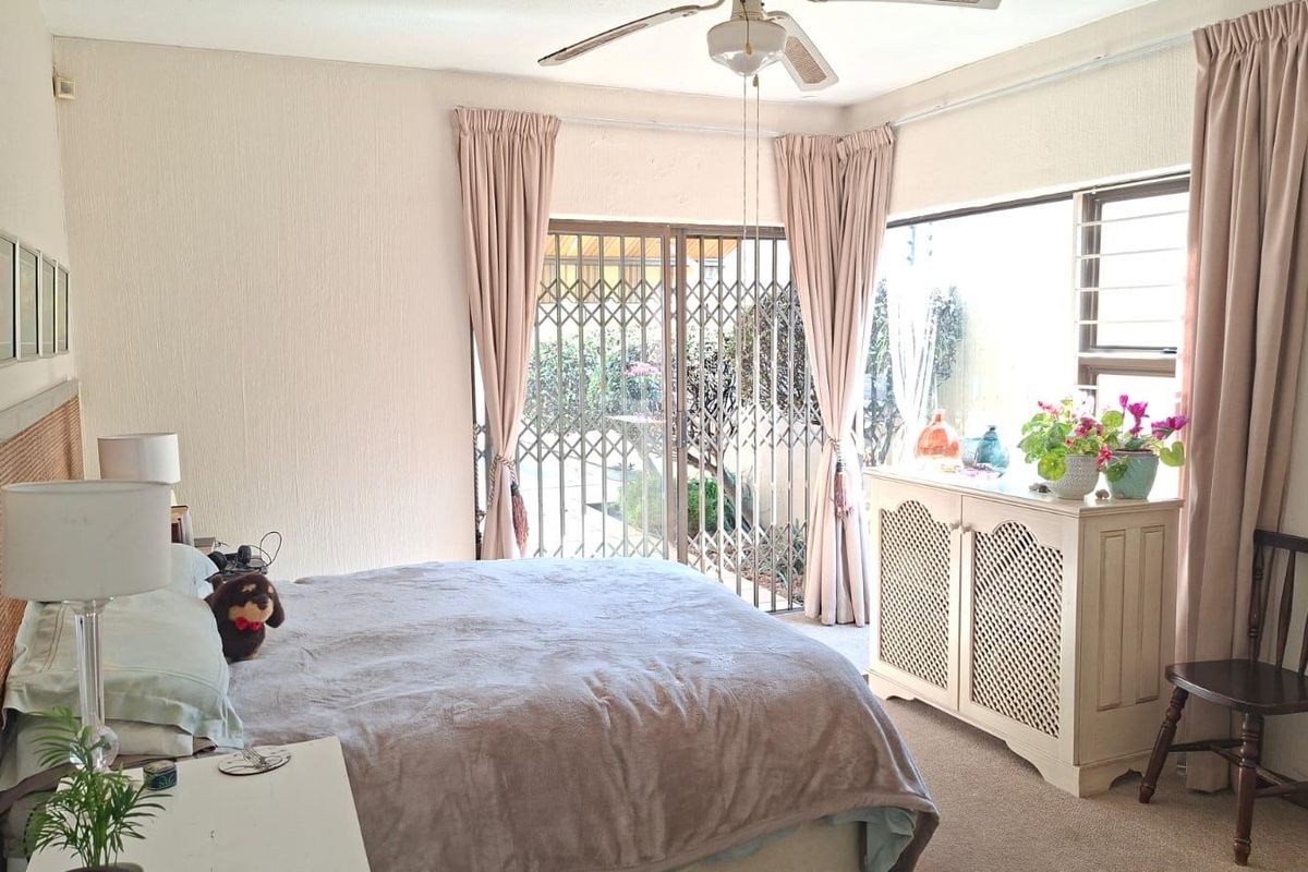 A bedroom featuring a ceiling fan, carpeted flooring, and a sliding glass door with a security gate leading to the exterior.