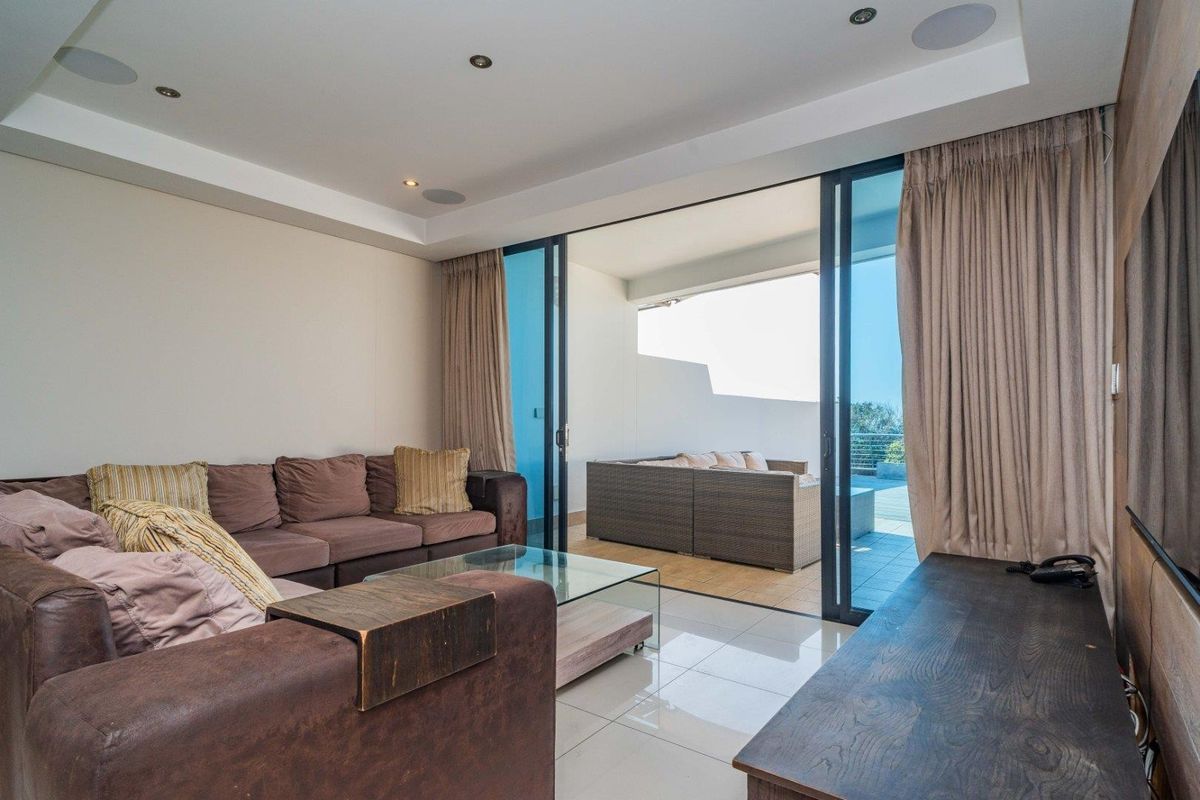 Modern living room featuring tiled flooring, recessed lighting, and large sliding glass doors that provide seamless access to the outdoor balcony area.