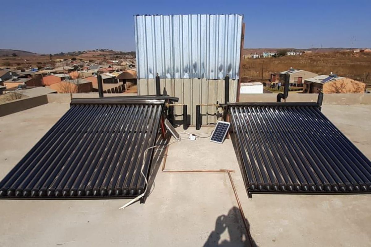 Rooftop view featuring two solar water heating collector panels and a corrugated metal enclosure for water storage infrastructure.