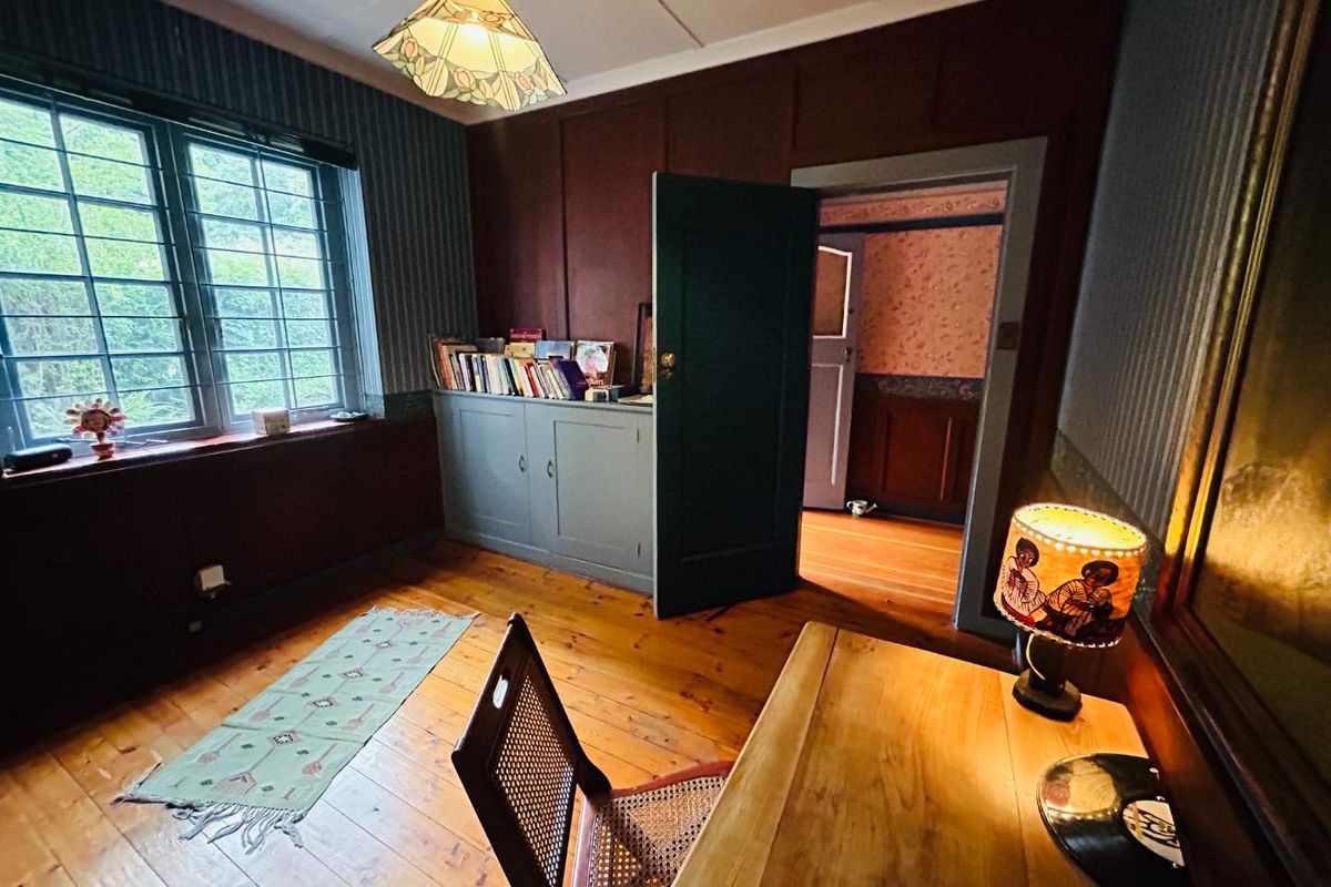 A cozy study or bedroom featuring timber flooring, built-in cabinetry, and a window with security bars, offering a warm and traditional aesthetic.