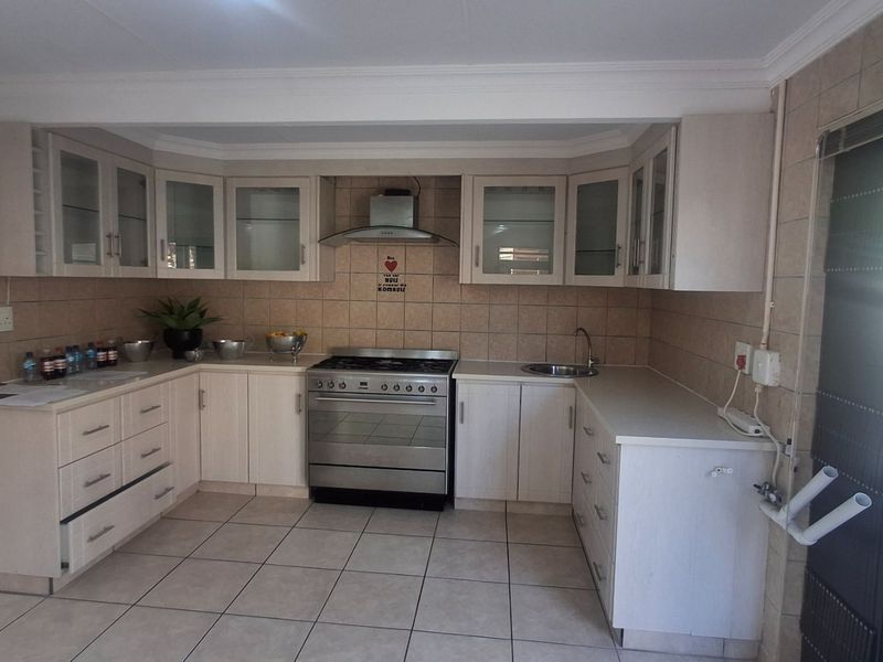 A functional kitchen featuring light-toned built-in cabinetry, a stainless steel stove with extractor fan, tiled backsplash, and tiled flooring.