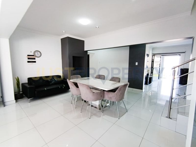Spacious open-plan living and dining area featuring polished porcelain floor tiles, modern downlighting, and a sleek stainless steel staircase railing.