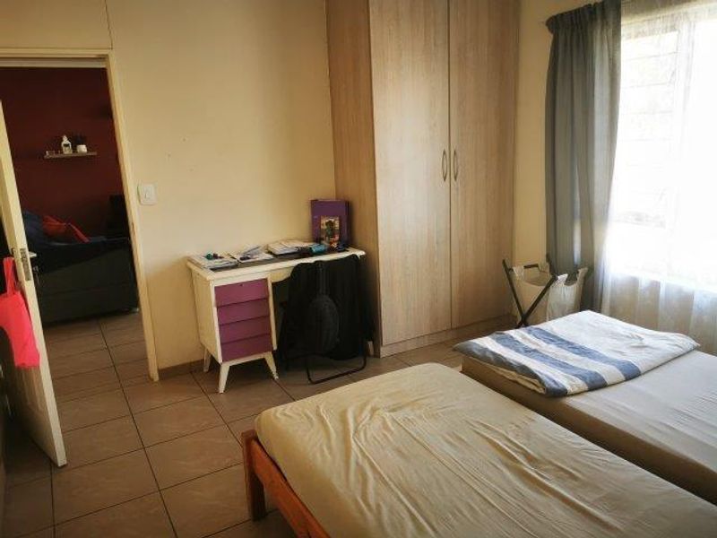 A functional bedroom featuring tiled flooring, a built-in wardrobe, and natural light from the window.