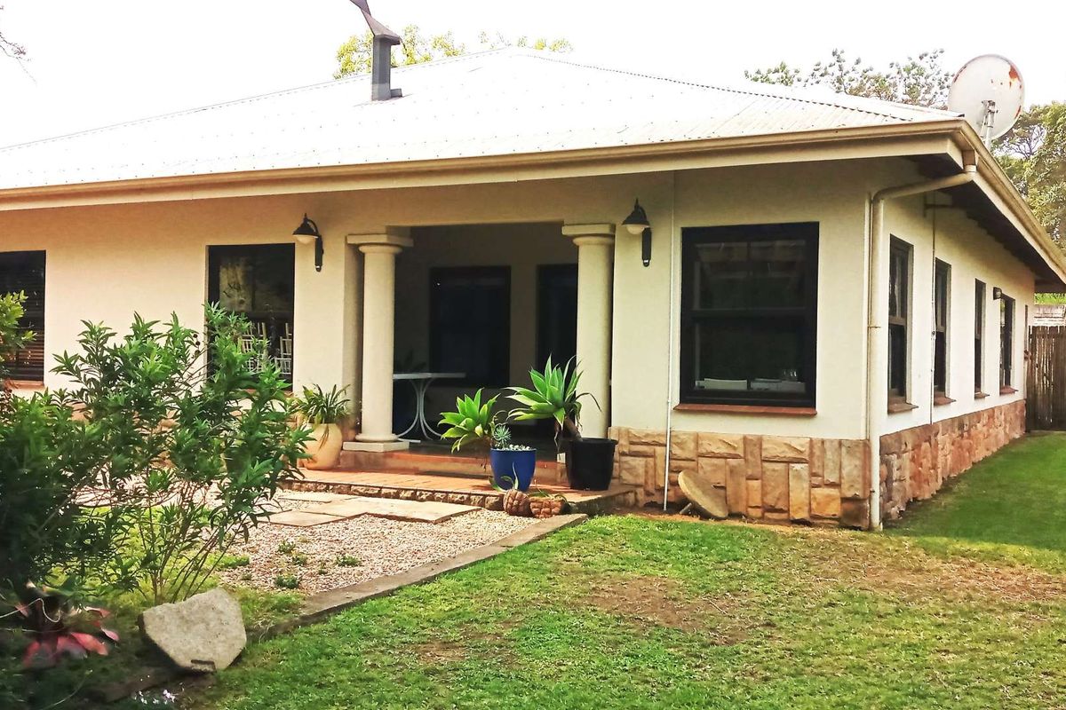 Rear view of a single-story residence featuring a covered patio with columns, stone cladding base, and a well-maintained garden area.