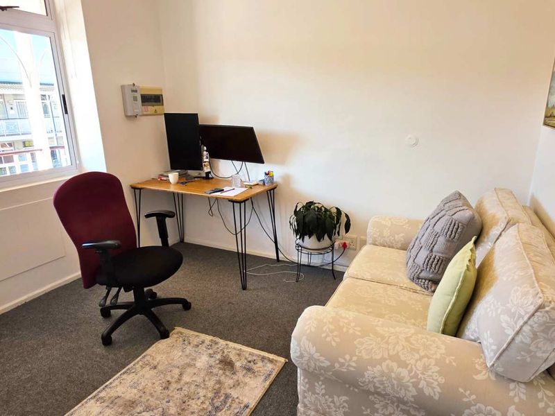A functional office space featuring carpeted flooring, a large window providing natural light, and a wall-mounted electrical distribution board.