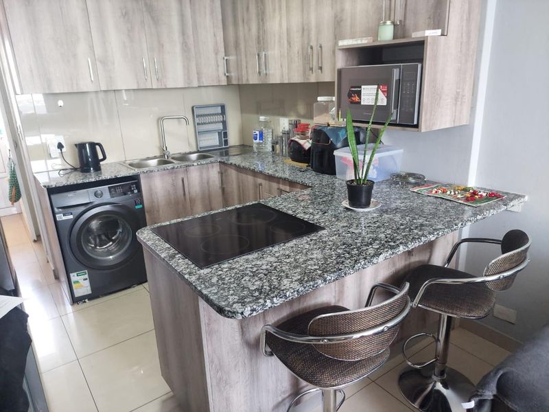 A functional kitchen featuring granite countertops, built-in cabinetry, an integrated electric hob, and a built-in microwave with tiled flooring.