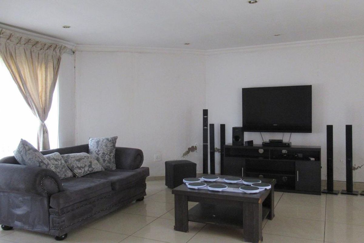 A living room featuring tiled flooring and recessed ceiling lighting, currently showing signs of wall surface wear and plaster damage.