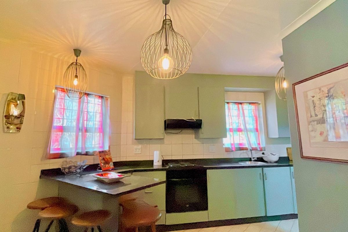 A functional kitchen featuring sage green cabinetry, dark countertops, a built-in oven with extractor fan, and a breakfast bar area.