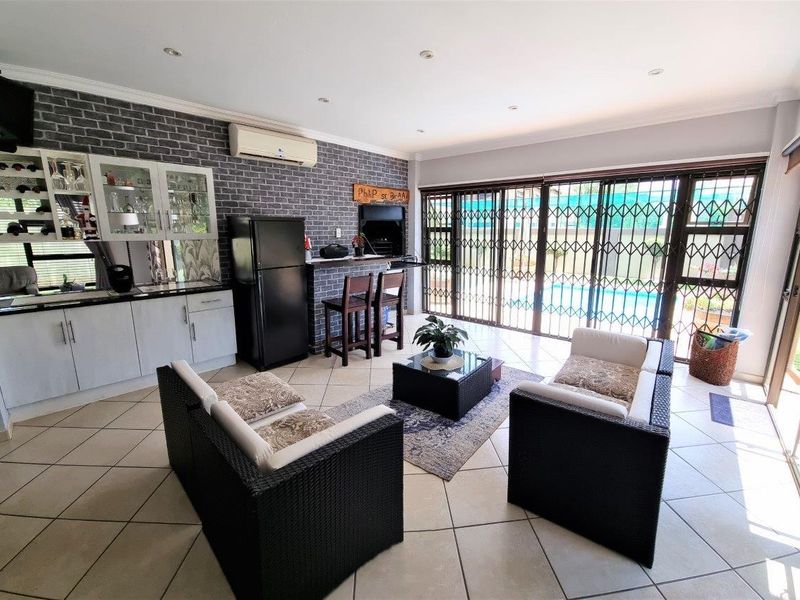 Open-plan living area featuring a built-in bar, indoor braai, tiled flooring, and large sliding doors providing direct access to the outdoor pool area.