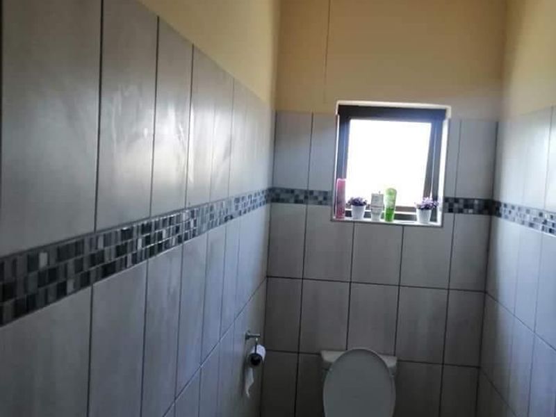 A functional bathroom featuring tiled walls with a decorative mosaic border, tiled flooring, and a top-hung window for natural light.