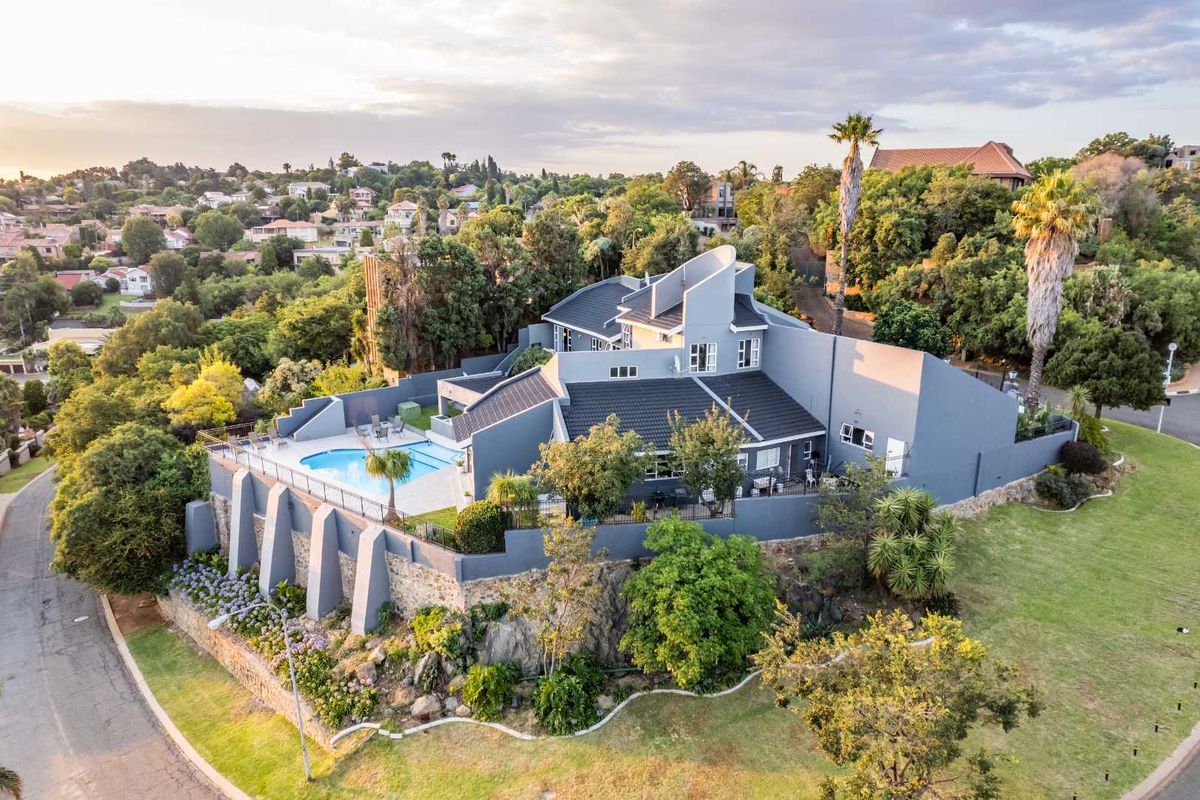 Aerial view of a modern multi-level residence featuring a swimming pool, expansive paved patio, and elevated retaining walls set within a landscaped suburban environment.