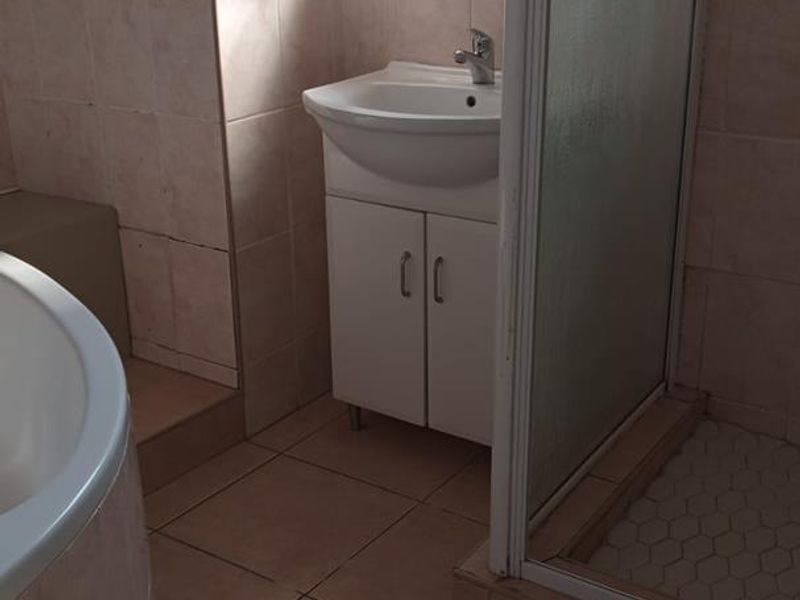 A dated bathroom featuring a vanity unit, shower enclosure, and bathtub with neutral wall and floor tiling.