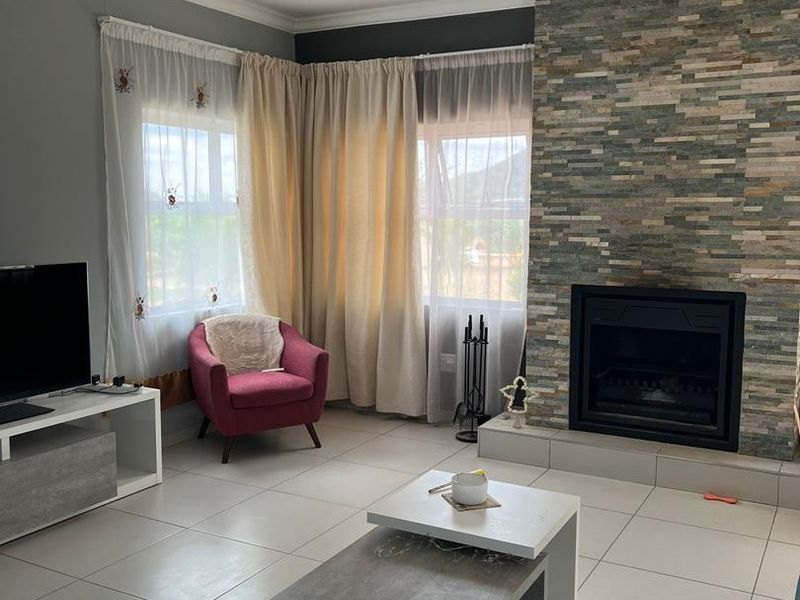 A comfortable living room featuring a prominent stone-clad fireplace, neutral tiled flooring, and large windows allowing for natural light.