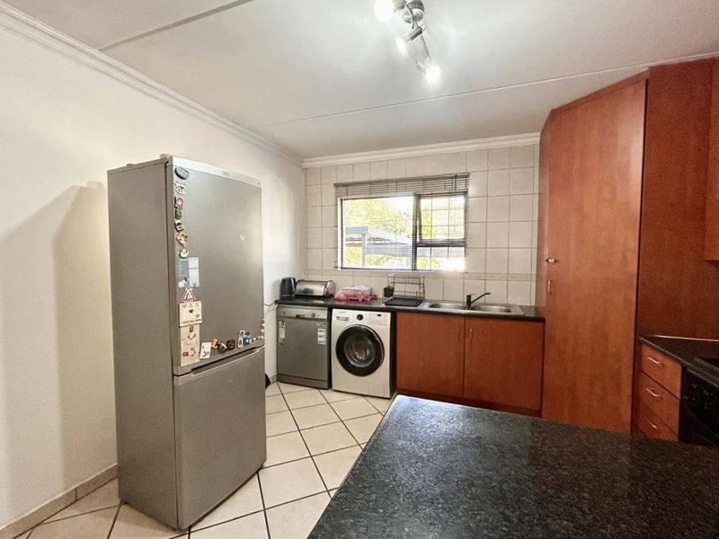 A functional kitchen featuring wood-finish cabinetry, dark countertops, a double sink, tiled backsplash, and tiled flooring with space for integrated appliances.