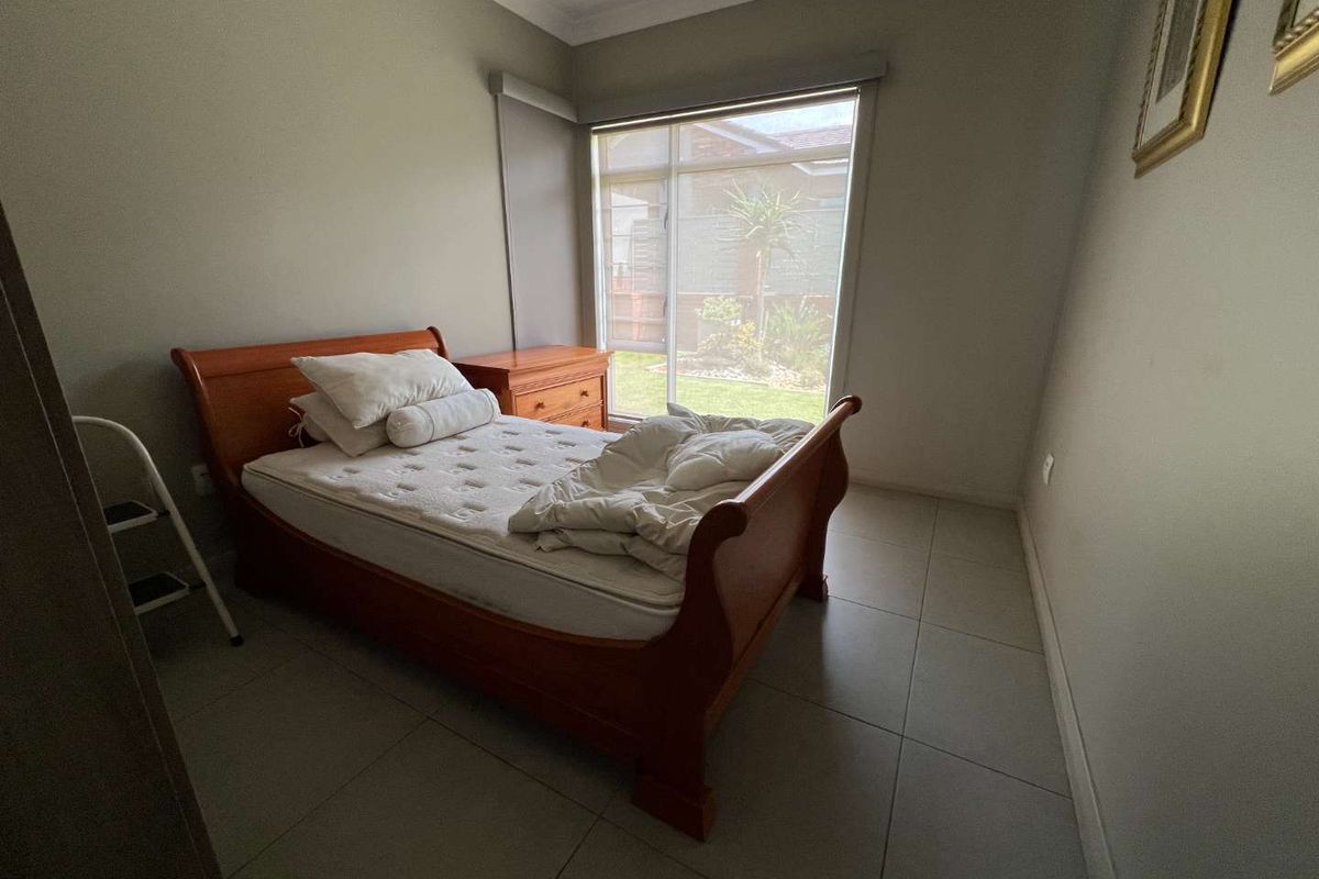 A bedroom featuring tiled flooring, neutral wall paint, and a large window providing natural light and a view of the garden.