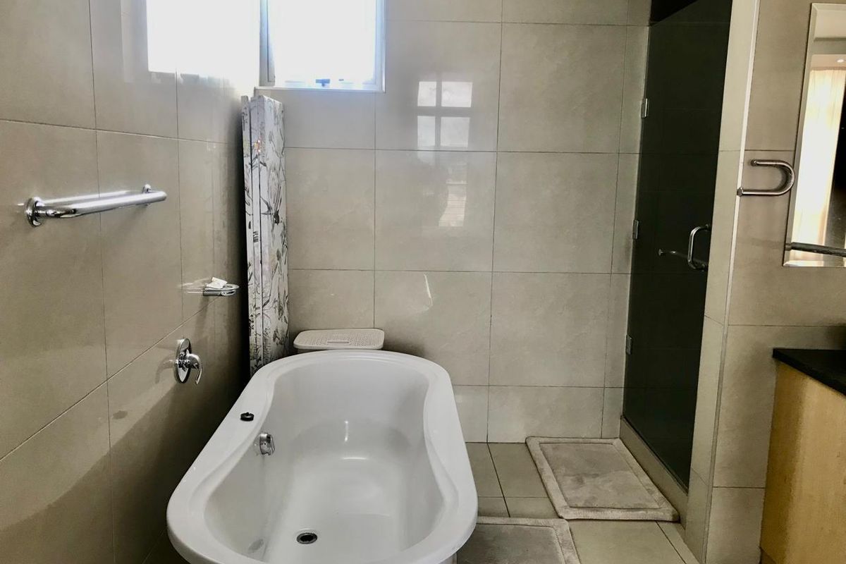 A modern bathroom featuring a freestanding bathtub, a separate glass-enclosed shower, and neutral wall tiling.
