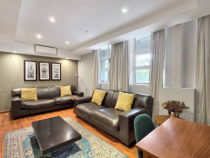 A well-lit living room featuring hardwood flooring, recessed downlighting, and a wall-mounted split-system air conditioner, offering a comfortable and functional living space.