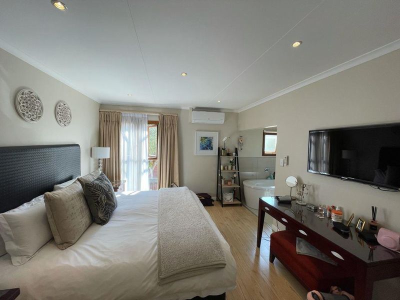 Spacious bedroom featuring laminate flooring, recessed lighting, a wall-mounted air conditioner, and an integrated en-suite bathtub area.