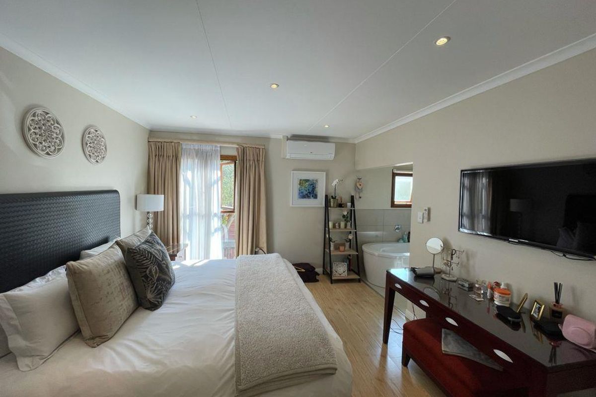Spacious bedroom featuring laminate flooring, recessed lighting, a wall-mounted air conditioner, and an integrated en-suite bathtub area.