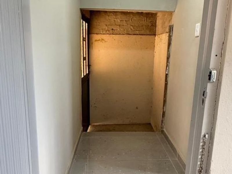 A narrow hallway featuring tiled flooring and coved ceilings, currently requiring finishing work on the walls and door frame.