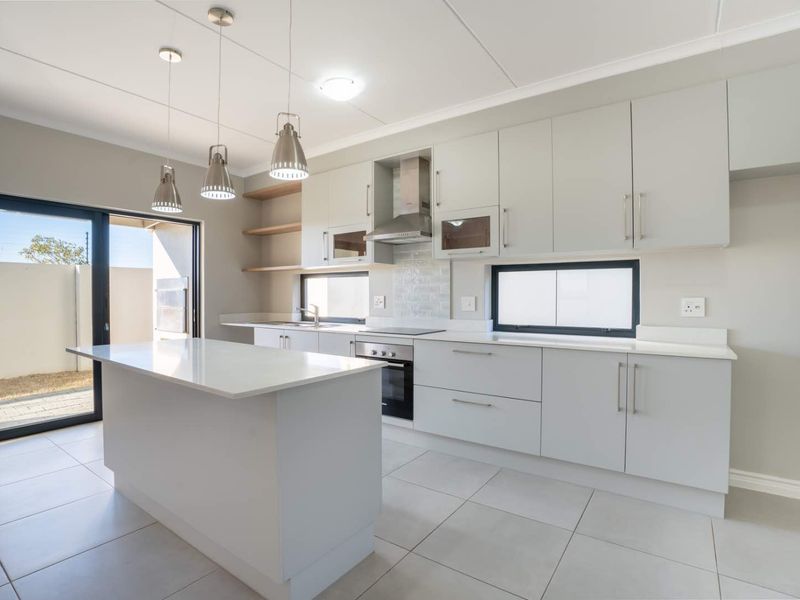 Modern kitchen featuring light grey cabinetry, stone countertops, a central island, built-in appliances, and direct access to an outdoor patio area.