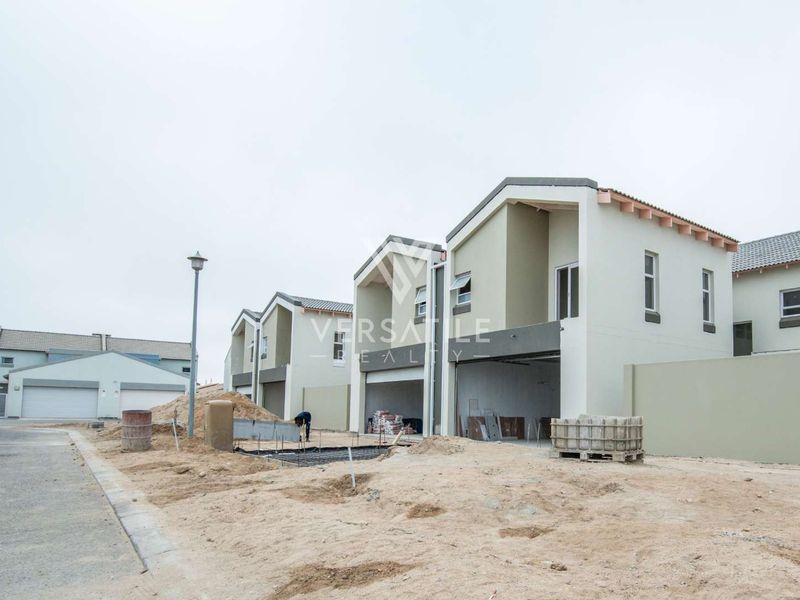 Exterior view of a townhouse development under construction, featuring modern architectural lines, tiled roofs, and unfinished surrounding grounds.