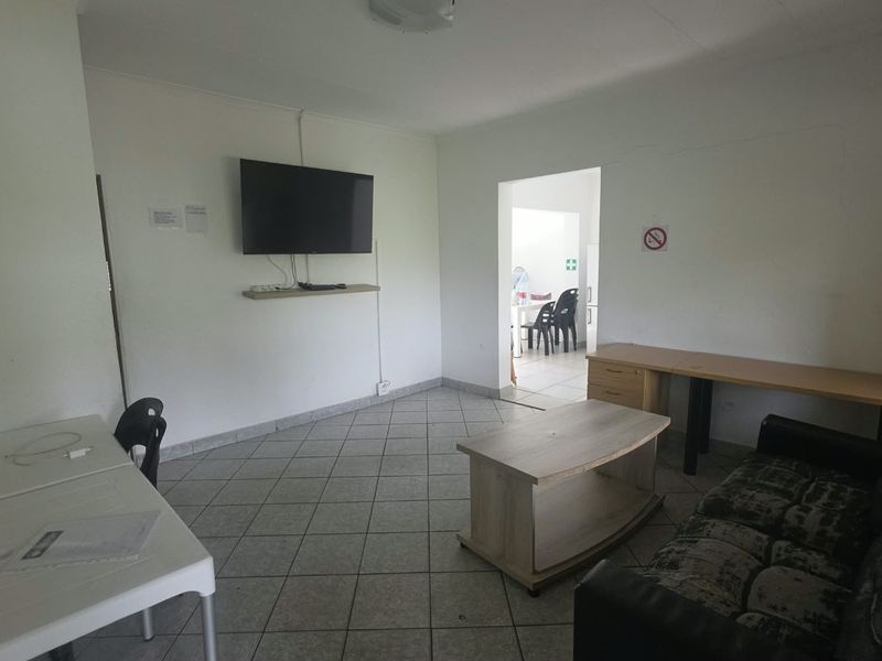 A functional living area featuring tiled flooring and a wall-mounted television setup, with an adjacent room visible through the doorway.