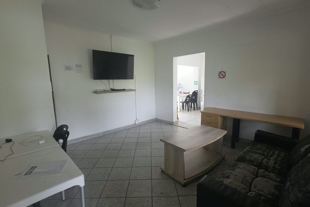 A functional living area featuring tiled flooring and a wall-mounted television setup, with an adjacent room visible through the doorway.