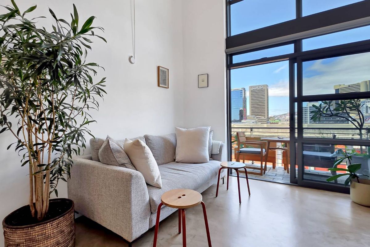 Bright living room featuring polished concrete floors, double-volume ceilings, and floor-to-ceiling windows with direct access to a private balcony and city views.