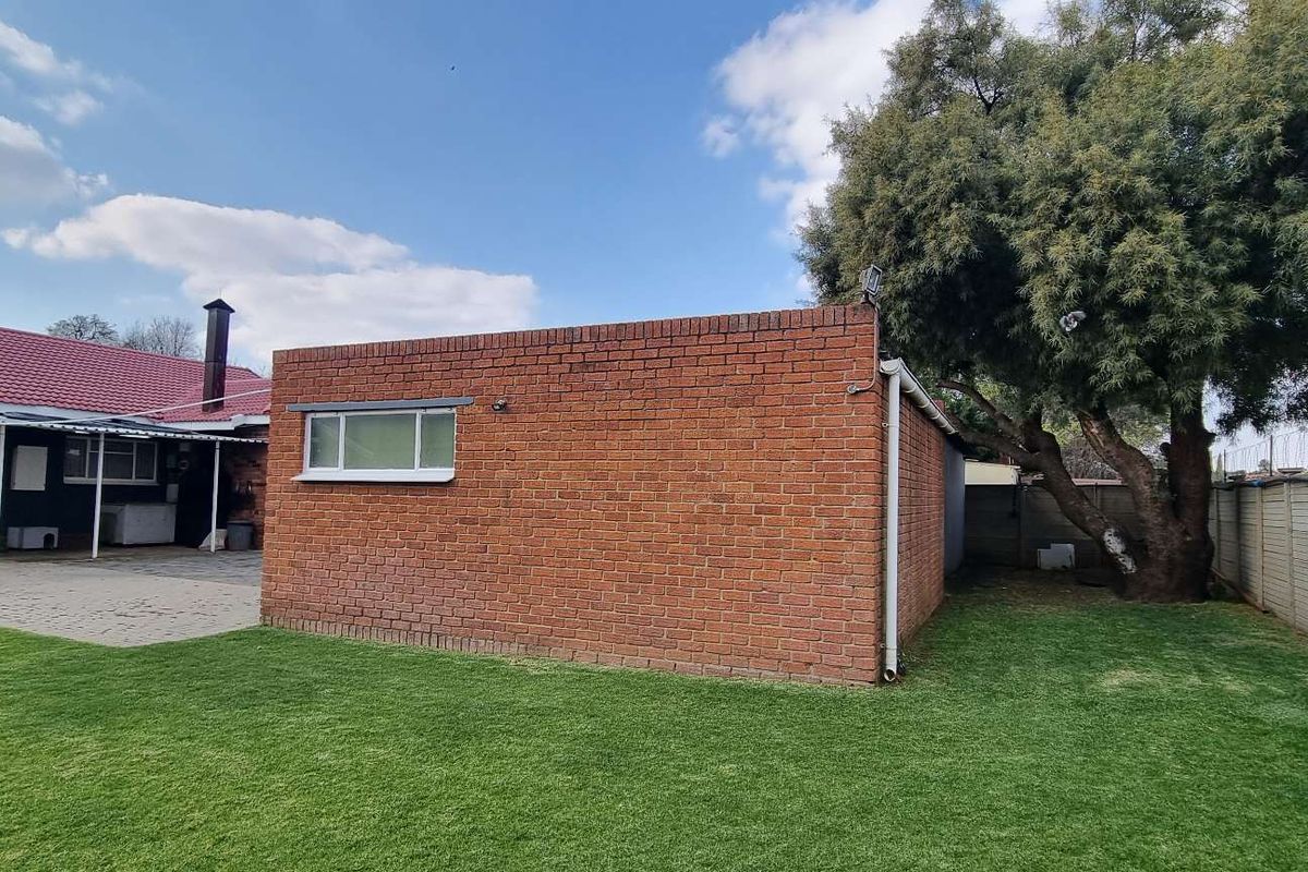 A view of the rear garden featuring a brick outbuilding, paved patio area, and established lawn with perimeter walling.