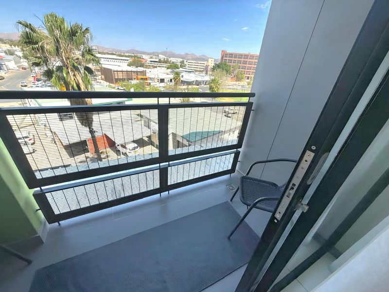 A compact balcony featuring tiled flooring and a modern metal balustrade, offering an elevated view of the surrounding urban area.