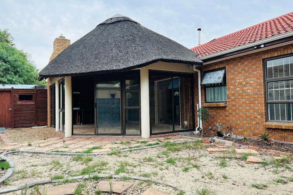 Rear view of the property featuring a distinctive thatched roof entertainment area, brick facade, and paved patio space.