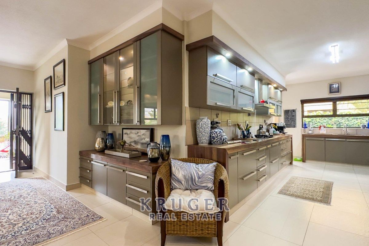 Modern kitchen featuring sleek built-in cabinetry, stone countertops, integrated appliances, and tiled flooring, with an adjacent service area and access to the exterior.