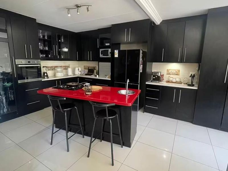 Modern kitchen featuring black cabinetry, a striking red island countertop, built-in oven, gas hob, and large format floor tiles.
