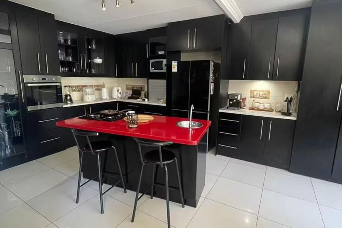 Modern kitchen featuring black cabinetry, a striking red island countertop, built-in oven, gas hob, and large format floor tiles.