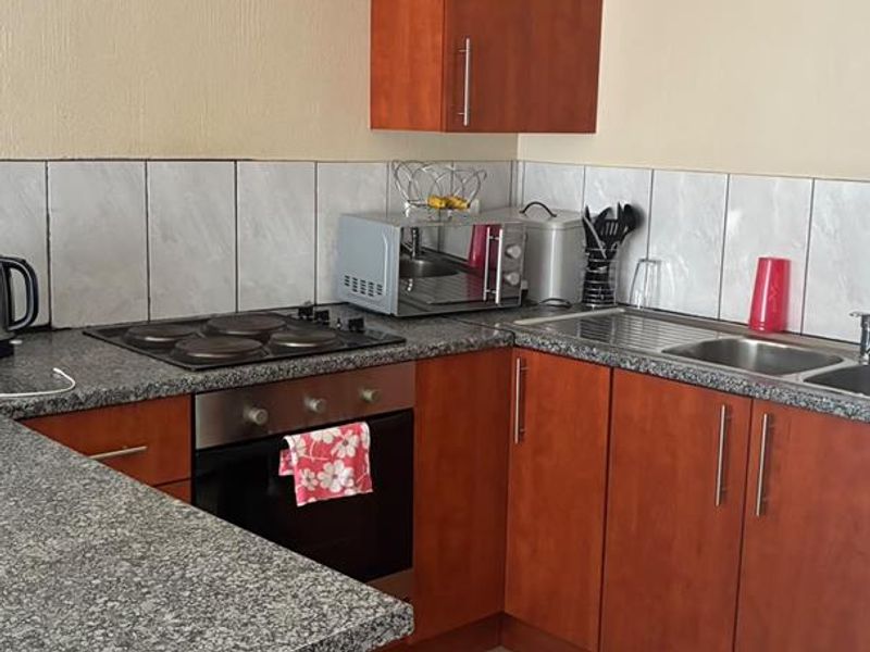 A functional kitchen featuring wooden cabinetry, granite countertops, a built-in oven with electric hob, and a tiled backsplash.