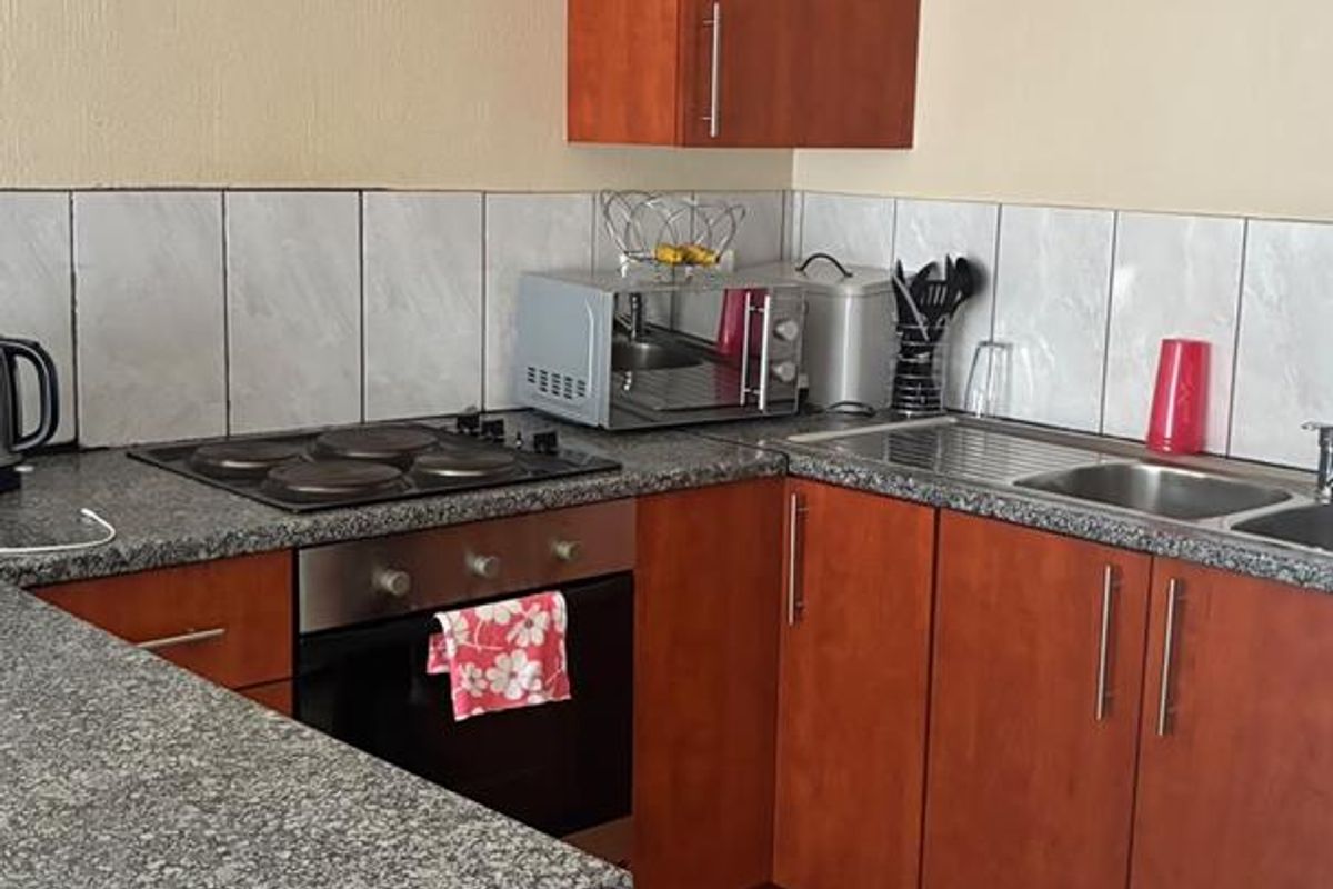 A functional kitchen featuring wooden cabinetry, granite countertops, a built-in oven with electric hob, and a tiled backsplash.