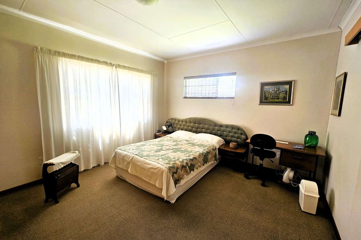 A spacious bedroom featuring neutral walls, carpeted flooring, and large windows with curtains, providing a comfortable and functional living space.