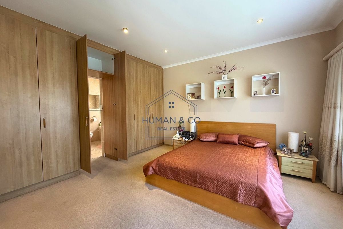 Spacious bedroom featuring extensive built-in wooden cupboards, recessed downlighting, and direct access to an en-suite bathroom.