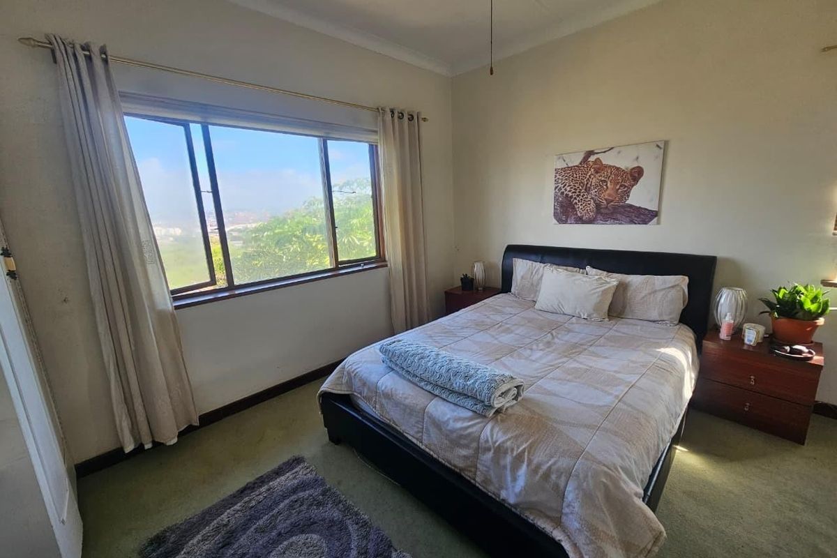 A bedroom featuring carpeted flooring, a large window with natural light, and a ceiling fan.