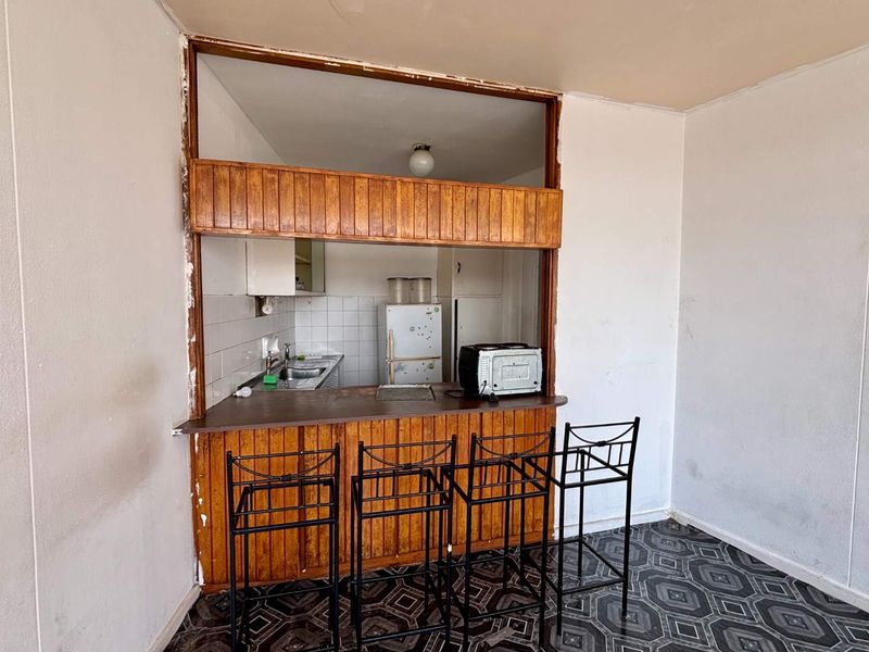 Open plan living area featuring a dated kitchen pass-through with a breakfast bar, tiled backsplash, and patterned flooring throughout.