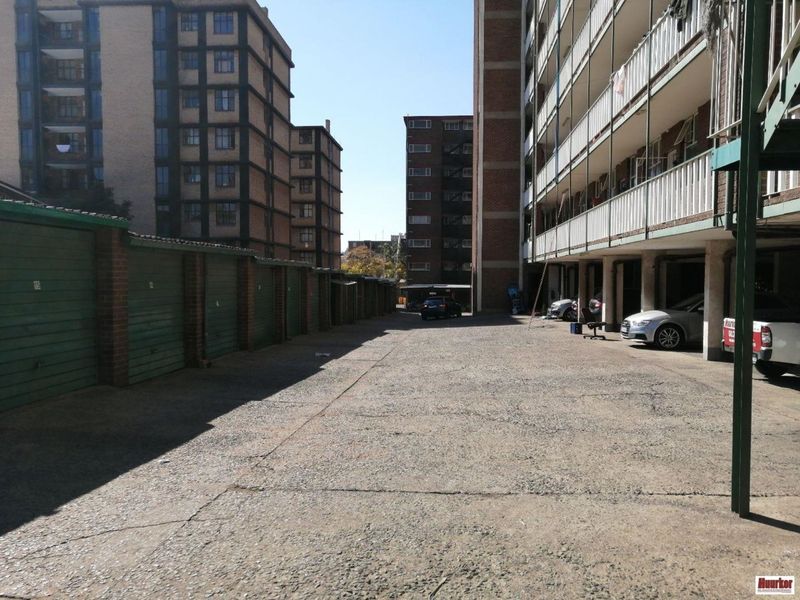 Exterior view of a residential apartment complex featuring a row of lock-up garages and a shared concrete parking area.