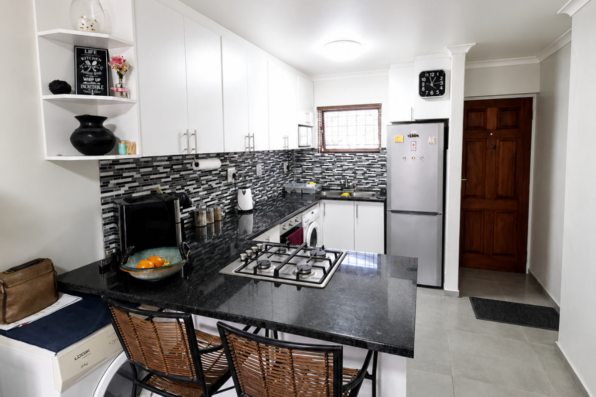 A functional kitchen featuring white cabinetry, granite countertops, a gas hob, and a modern mosaic tile backsplash with integrated laundry appliances.