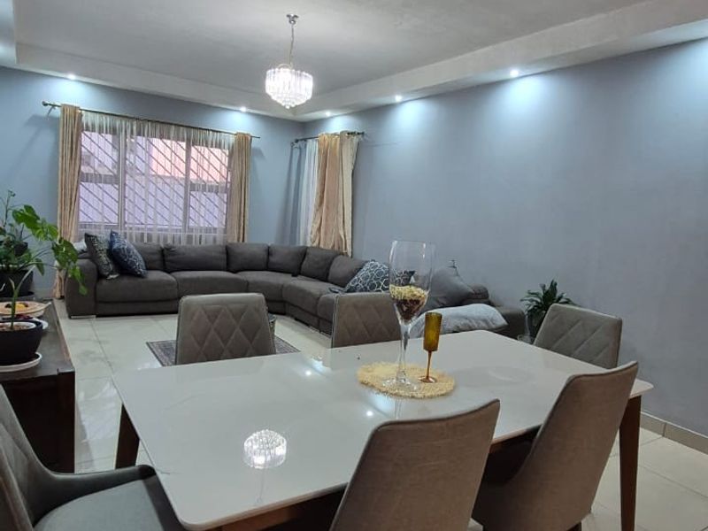 Spacious open-plan living and dining area featuring neutral tiled flooring, recessed ceiling lighting, and a modern pendant light fixture.