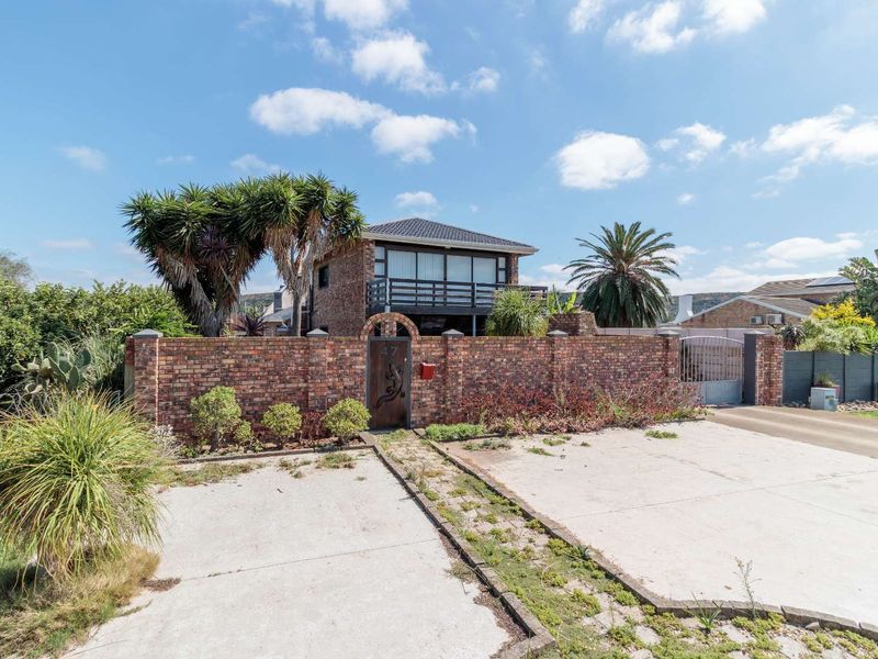 Front exterior view of a double-story brick house featuring a balcony, enclosed brick boundary wall, and a concrete driveway.