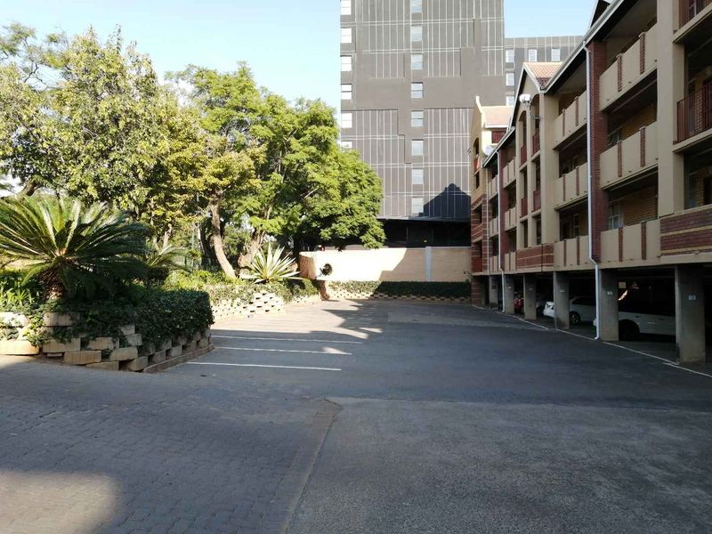 Exterior view of the apartment complex featuring a paved driveway, covered parking bays, and established garden landscaping.