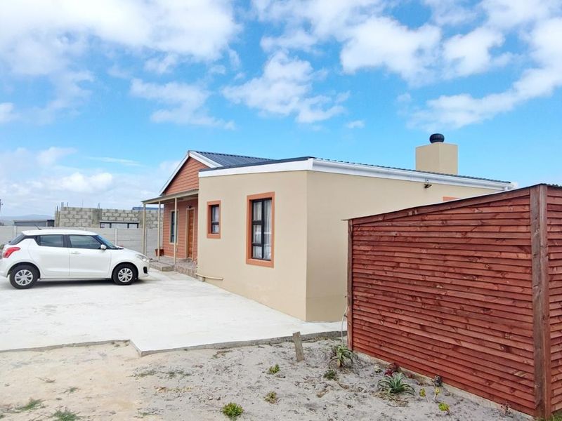 Front view of a single-story house featuring a concrete driveway, timber cladding, and a metal roof with a chimney.